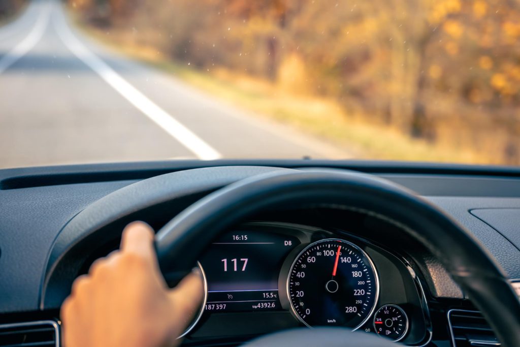 Driver's view through the windscreen with hands on the steering wheel and speedometer visible on an open road